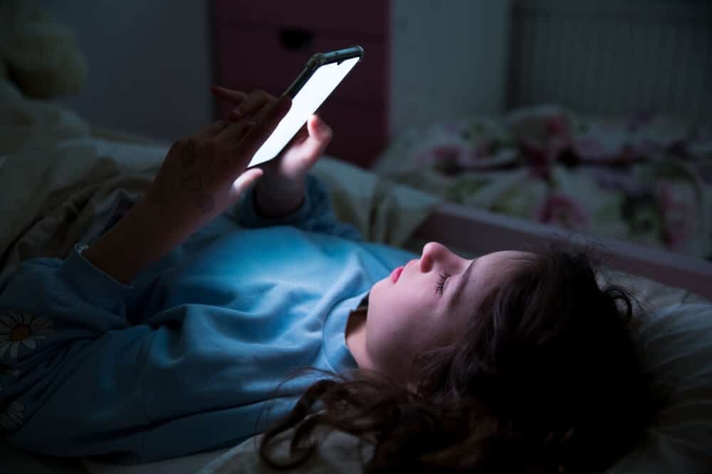 A child lying in bed using a smartphone at nighttime